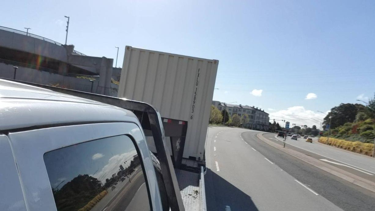 shipping container on flat bed truck shipped to location street highway storage container blue sky cloudy