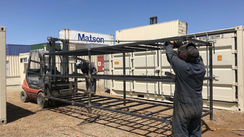 workers constructing container frame blue sky black outfit black metal bars cream color shipping container storage containers